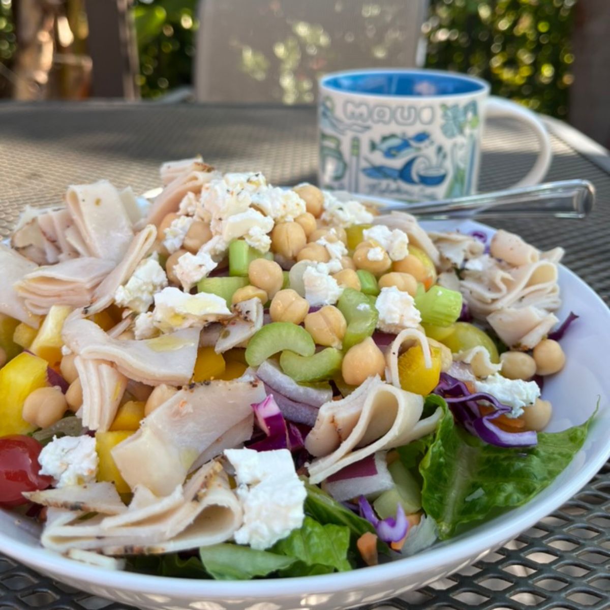 large bowl of salad on patio table with a maui mug in the background.