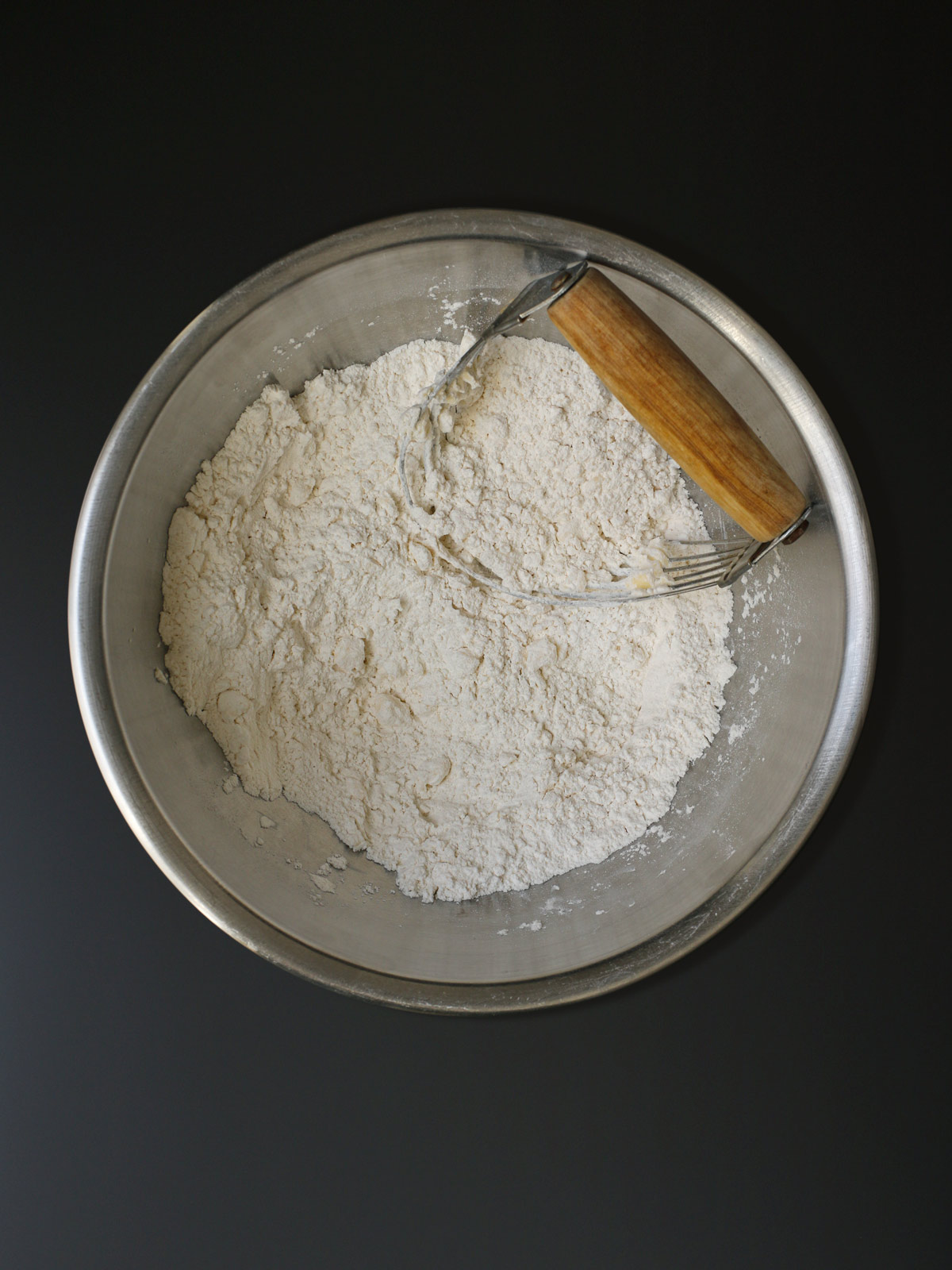 pastry blender in bowl with flour and butter worked into crumbs.