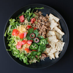 turkey taco salad in a black bowl, with toppings.