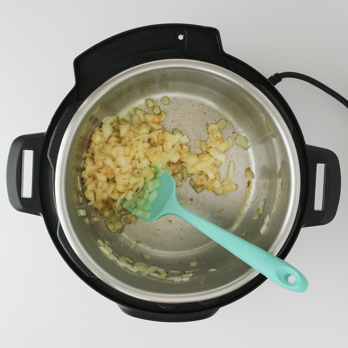 onions sauteed in pressure cooker insert with teal spatula.