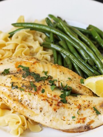 close up of sauteed tilapia with herb butter, green beans, and buttered noodles.