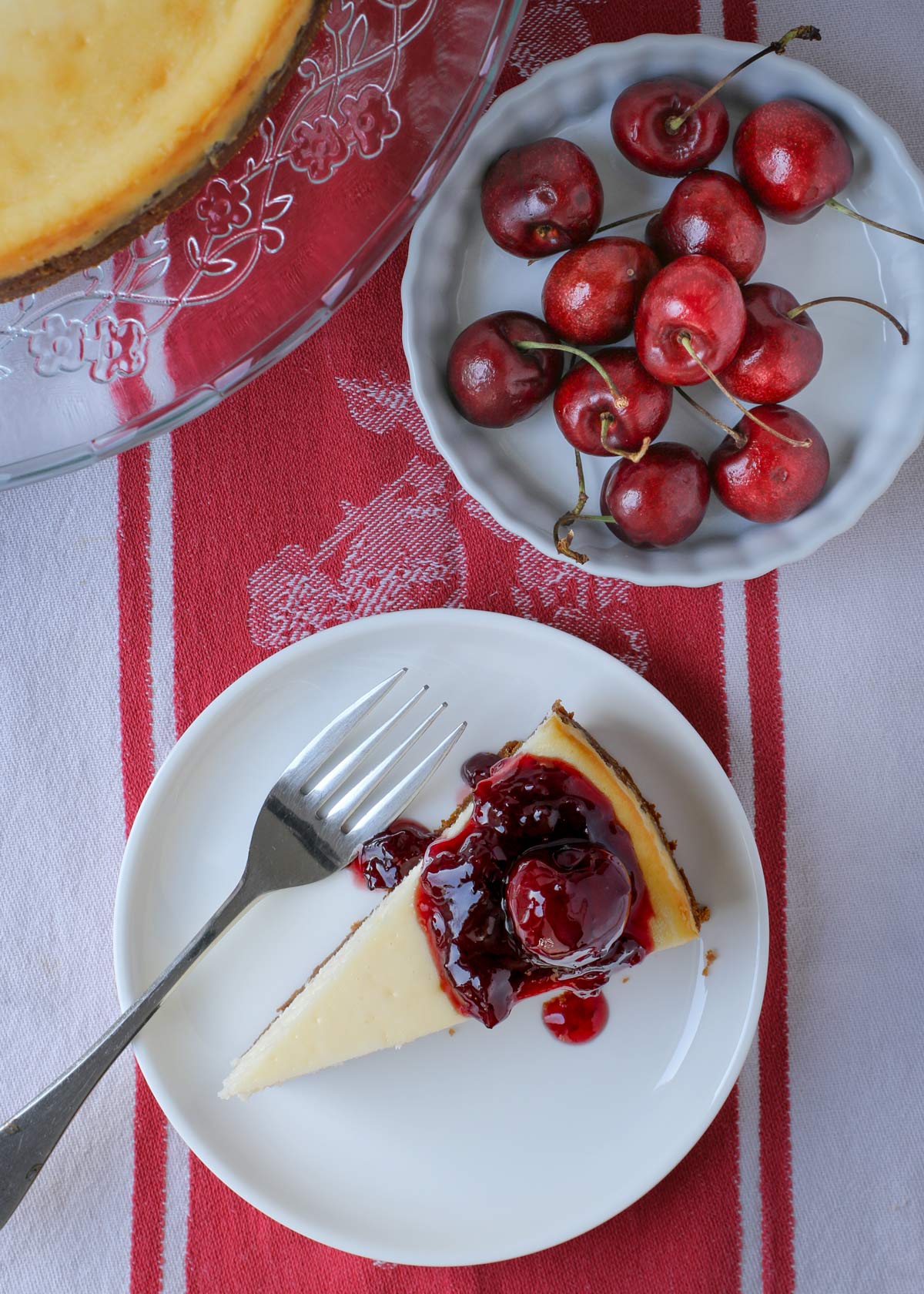 overhead shot of cheesecake on plate with cherries in a dish nearby.