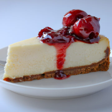 slice of cherry cheesecake on a white plate on a white table.