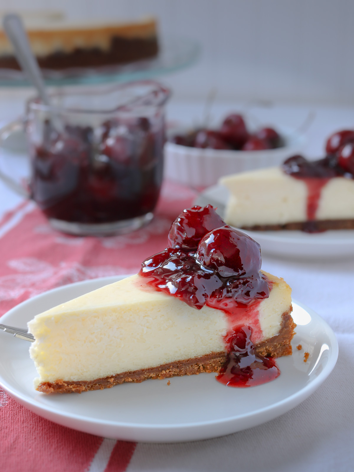 slices of cherry cheesecake on dessert plates with red cloth on table.