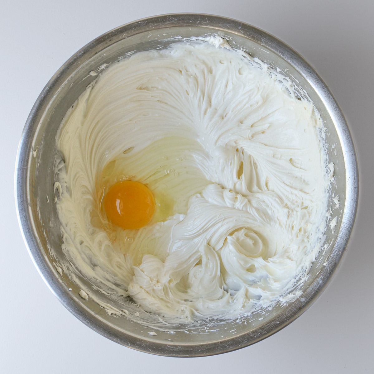 adding eggs to cream cheese mixture in mixing bowl.