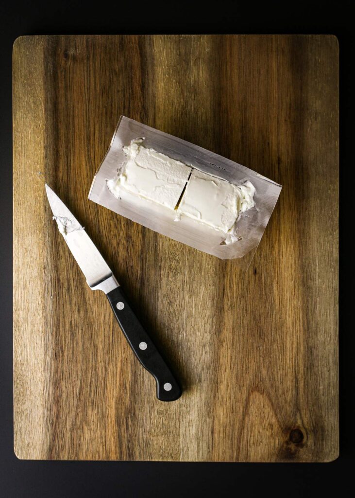 log of cheese cut in half  with knife on cutting board.