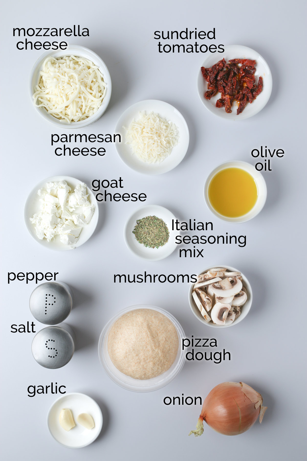 ingredients for goat cheese pizza laid out on white table.