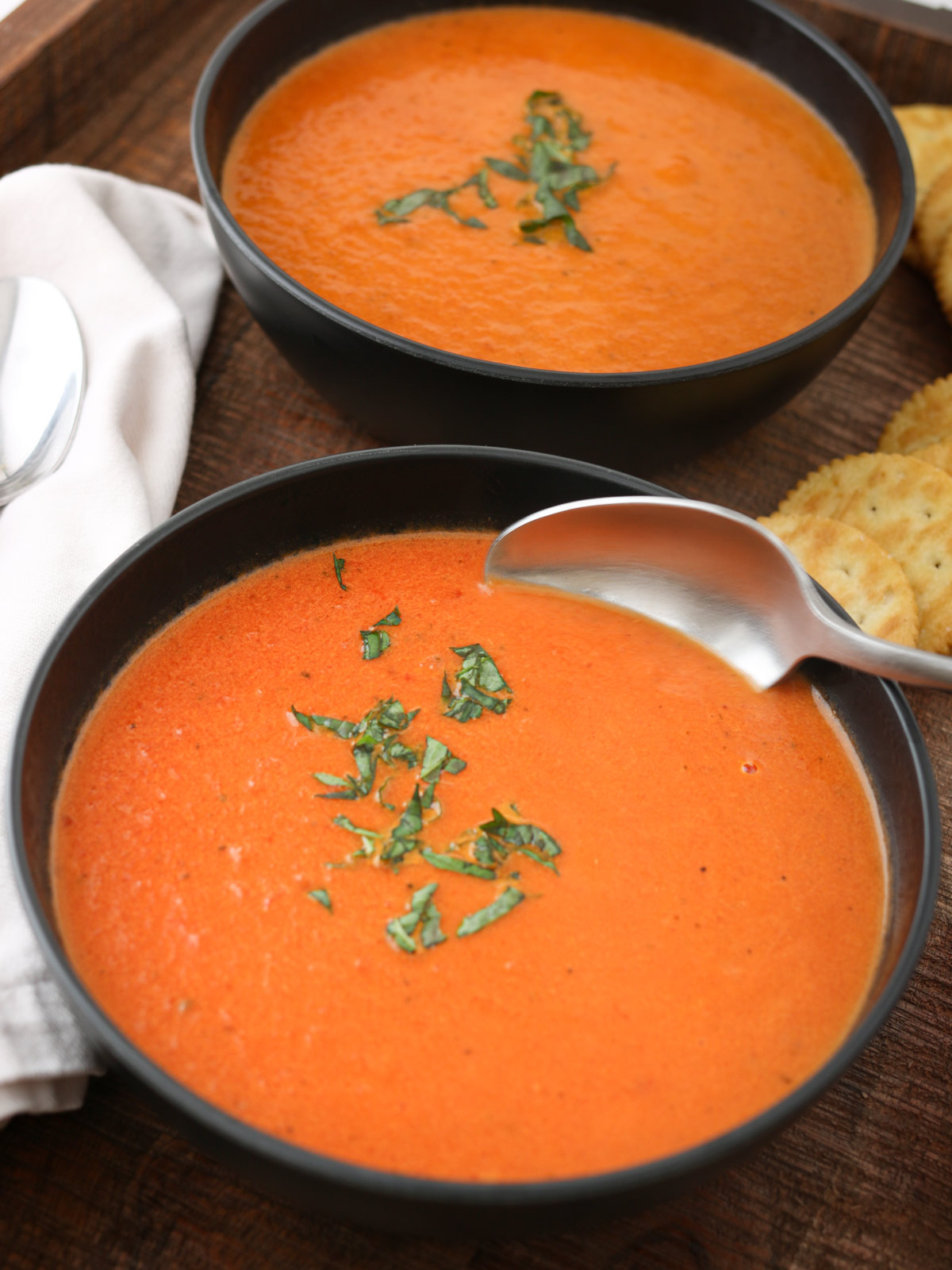 dipping a spoon into tomato soup in black bowl.
