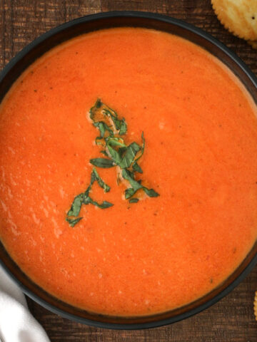 overhead shot of tomato soup in black bowl with basil garnish.