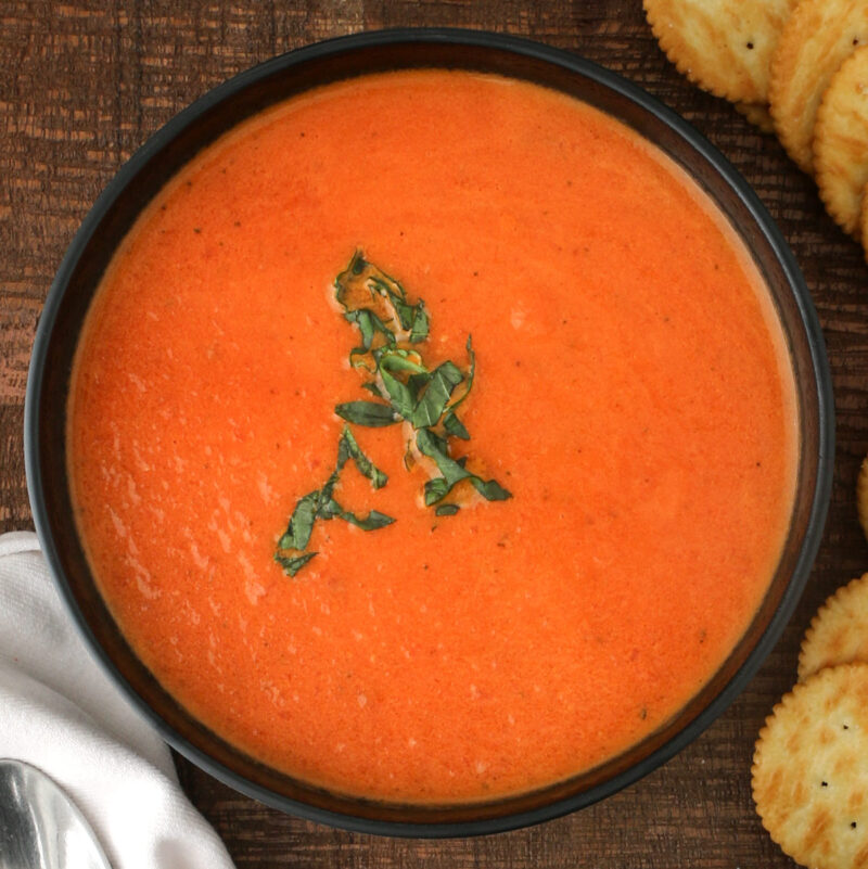 overhead shot of tomato soup in black bowl with basil garnish.