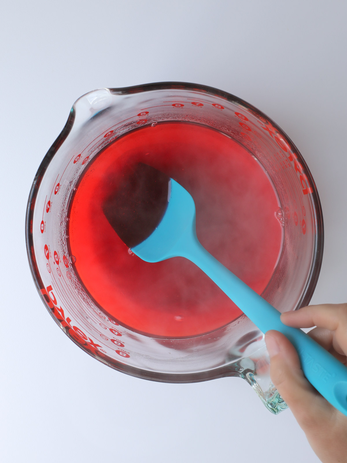 stirring gelatin and hot water with teal spatula in glass bowl.