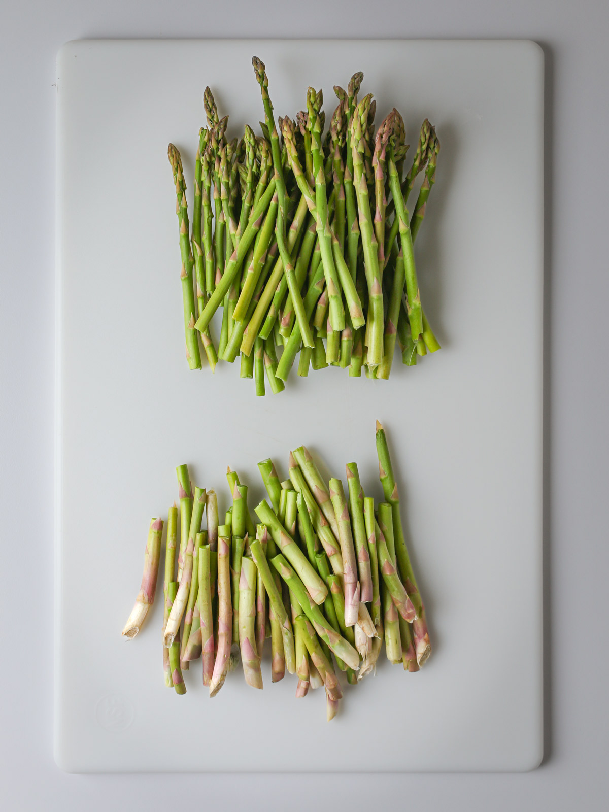 asparagus spears on a white cutting board with the woody stems broken off in a pile.