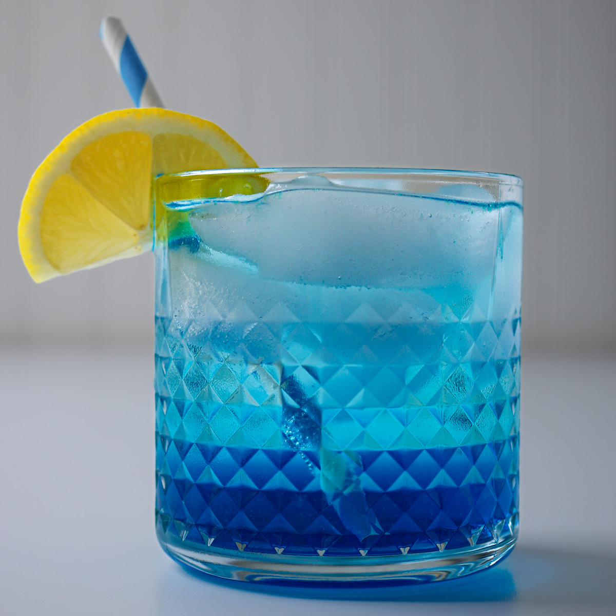 side view of a blue lagoon mocktail with lemon wedge and blue straw.