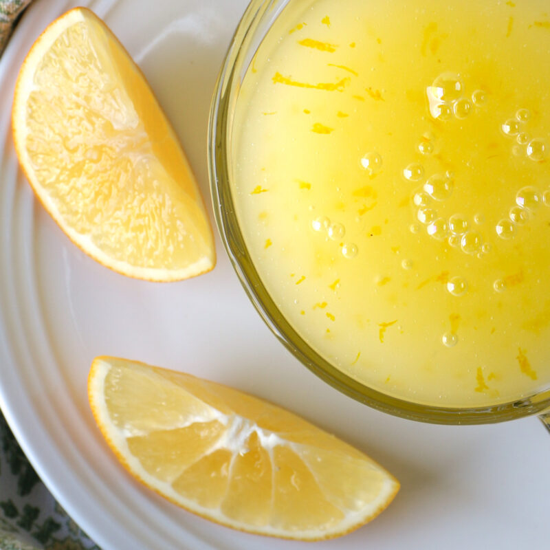 overhead shot of lemon wedges and a small pitcher of lemon sauce on a white platter.