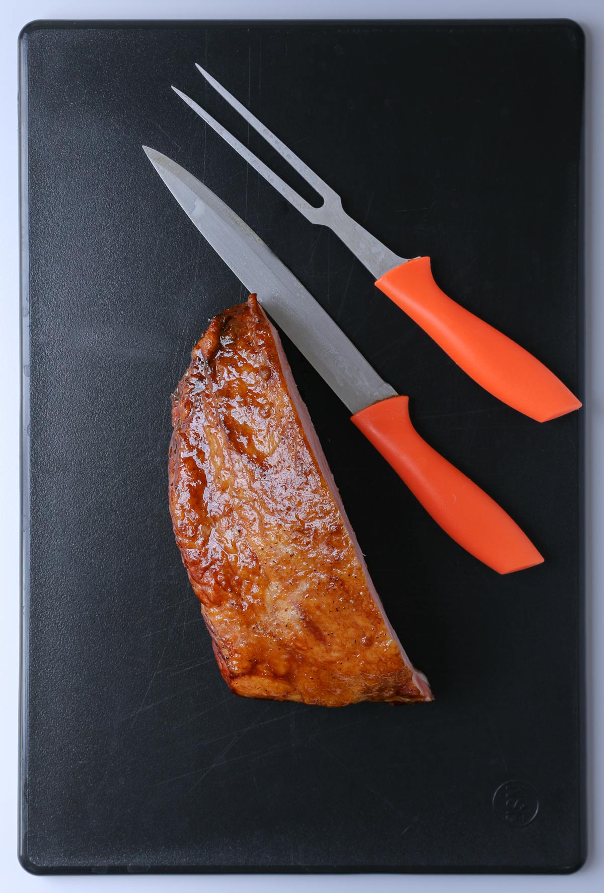 leftover ham on a black cutting board with a knife and carving fork.