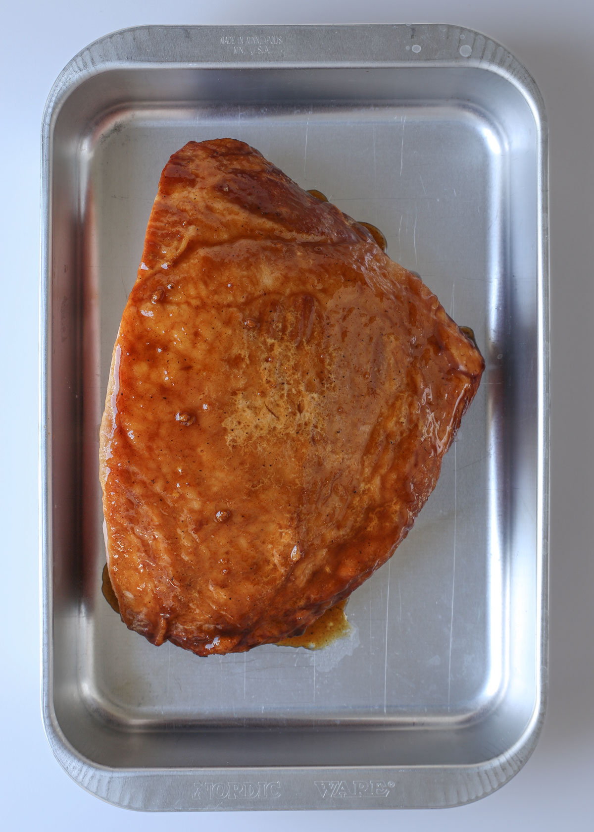 glazed half ham in a baking pan on a white table.