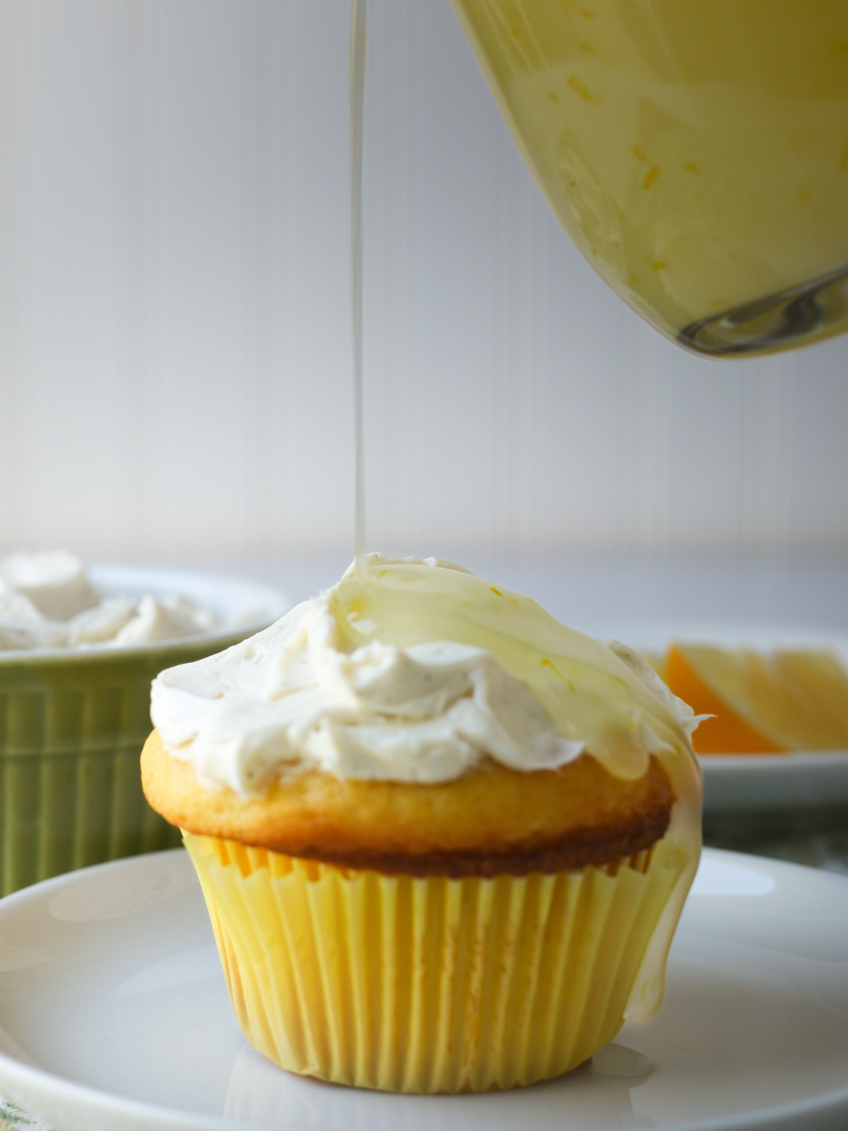 pouring lemon sauce over a cupcake topped with sweet cream cheese.