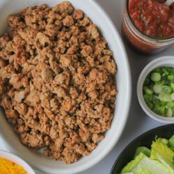 cooked taco meat in oval dish with taco toppings nearby.