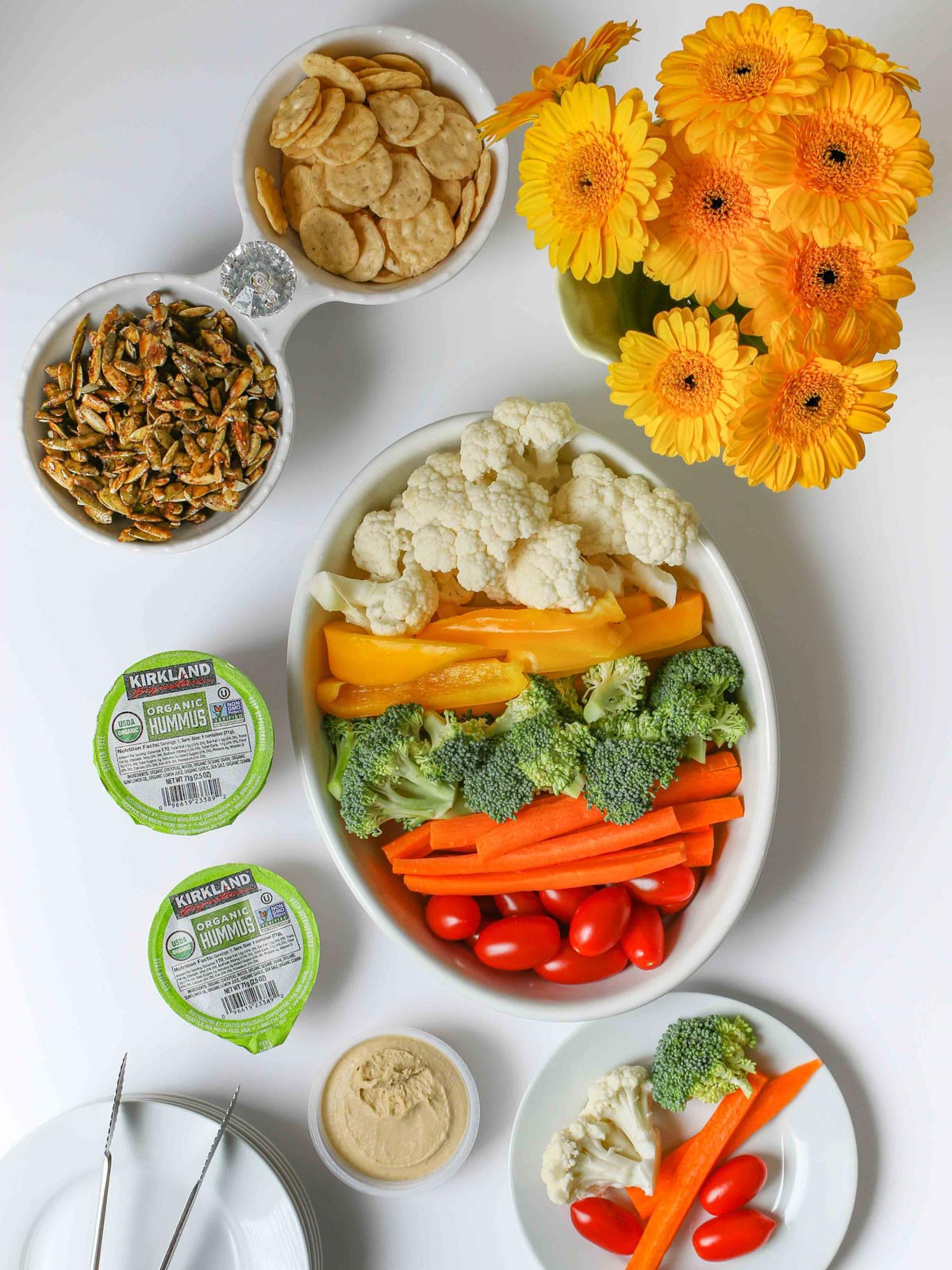Easter egg veggie tray on table with other apps and small cups of hummus, with flowers.