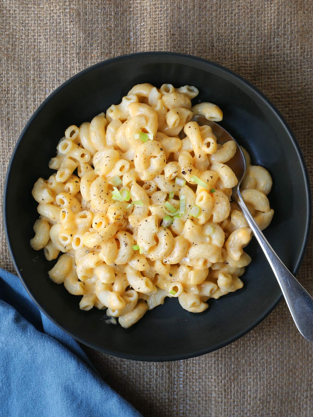 black bowl of macaroni and cheese topped with green onion, with a spoon.