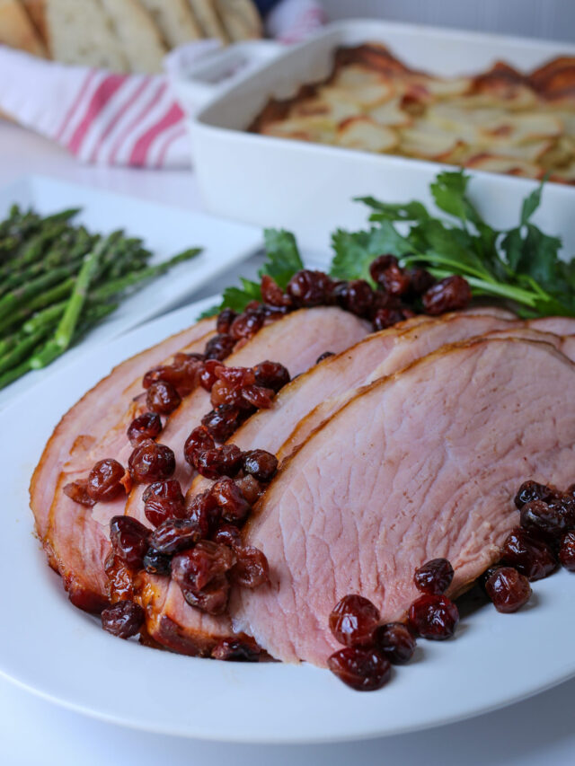 dinner table set with platters of ham, potatoes, asparagus, and a bread basket.
