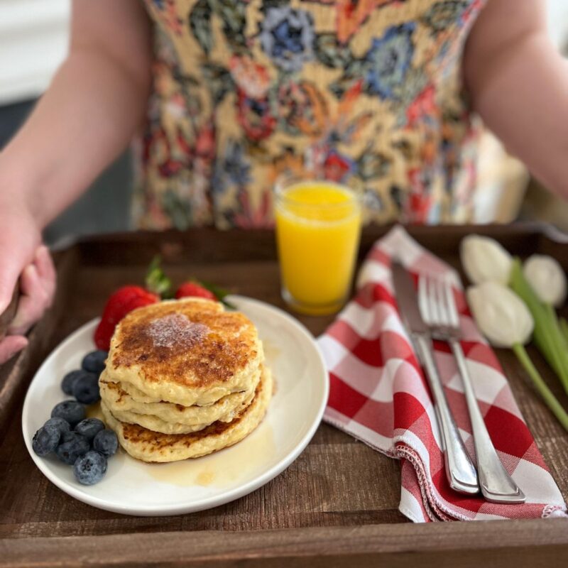 woman holding breakfast tray with plate of pancakes.