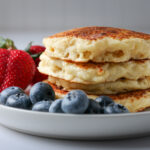 stack of eggless pancakes on plate with strawberries and blueberries.