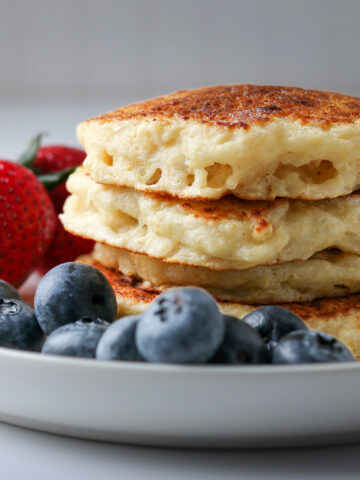 stack of eggless pancakes on plate with strawberries and blueberries.