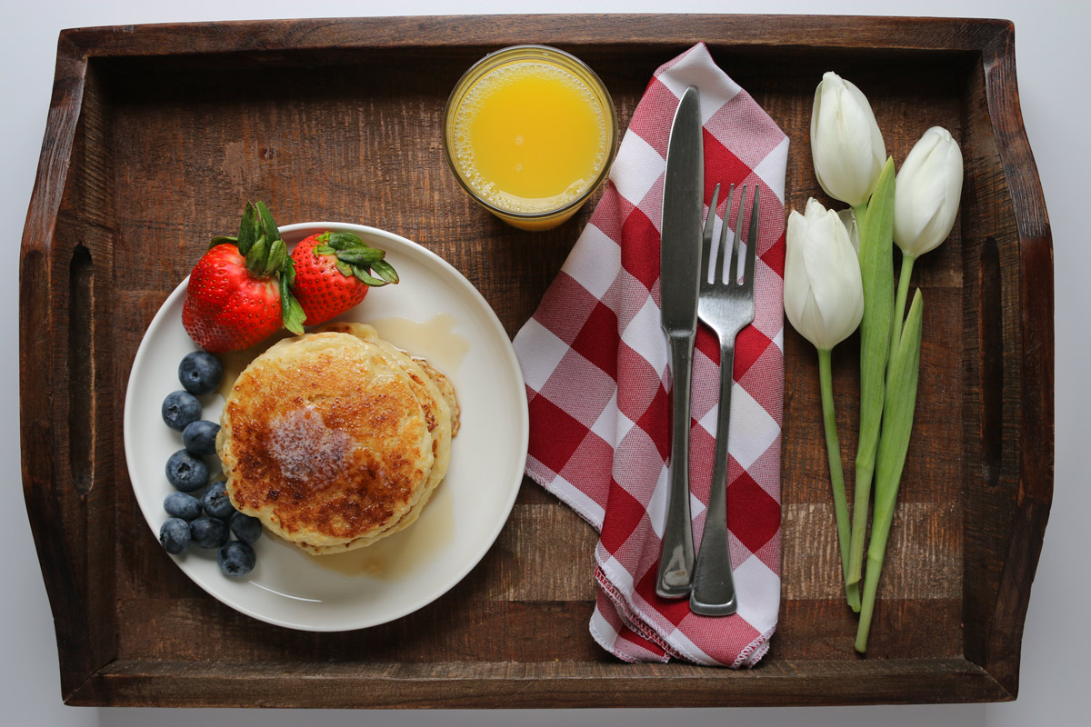breakfast tray laden with a plate of pancakes, orange juice, and tulips.