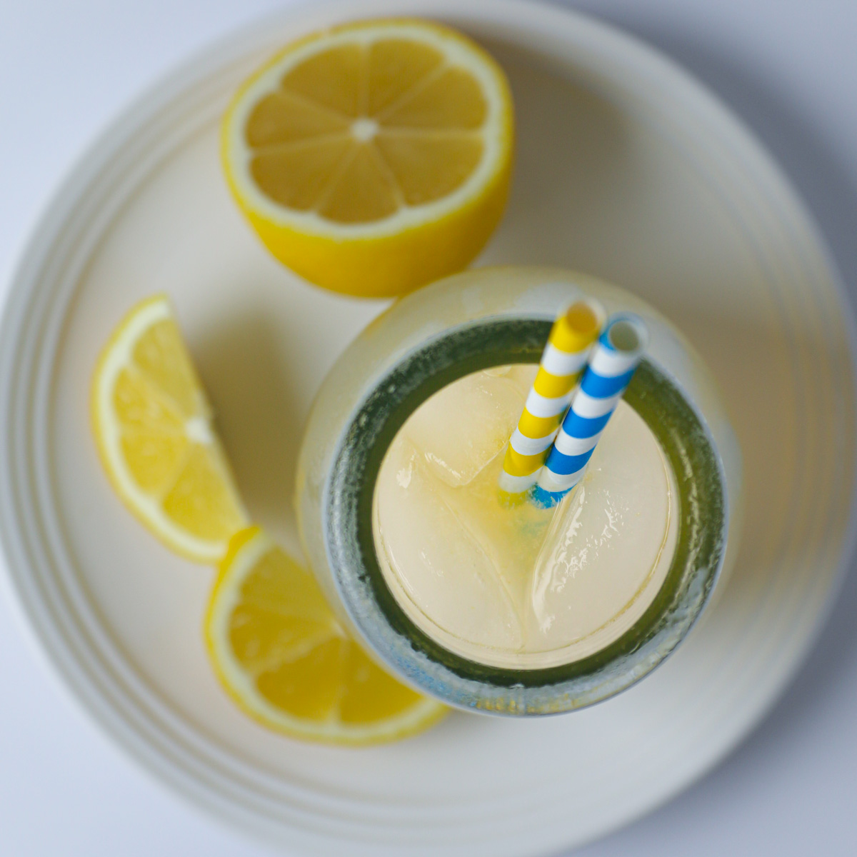overhead shot of glass of lemonade on plate with cut lemon and wedges.