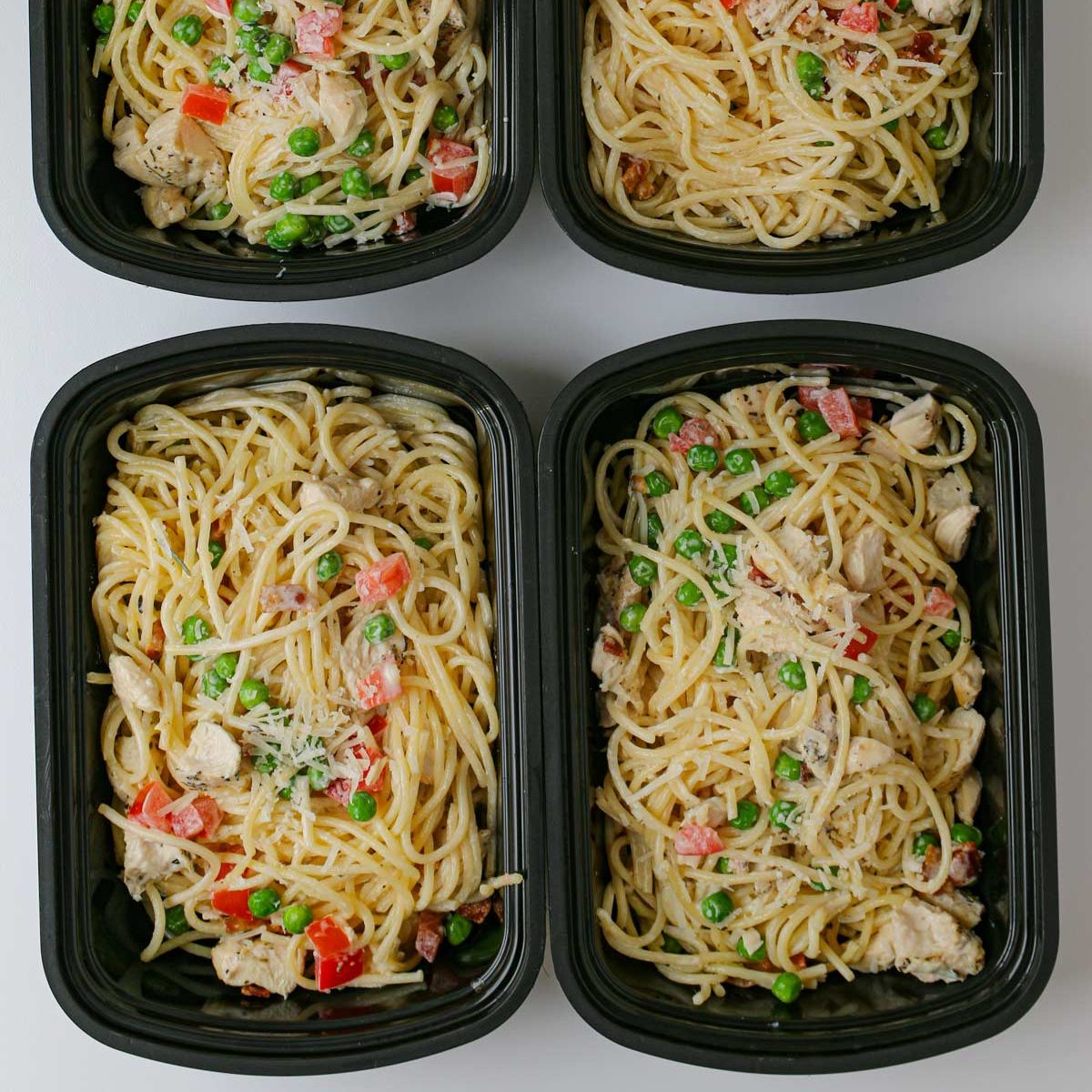 meal prep boxes full of a gourmet pasta dish, laid out on a white table.