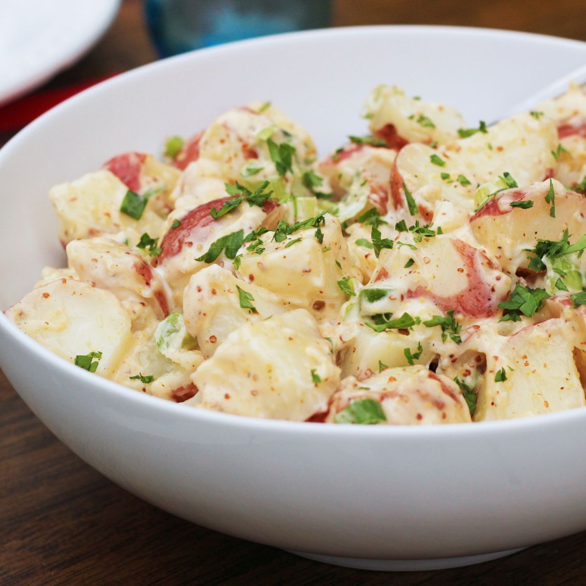 white bowl with red potato salad topped with fresh parsley.