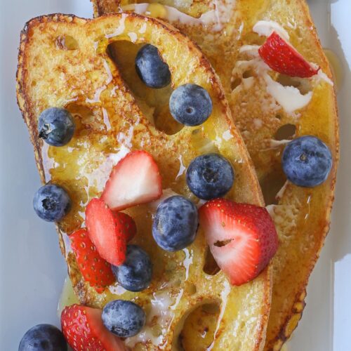 close up of two slices of sourdough french toast topped with butter, honey, and berries.