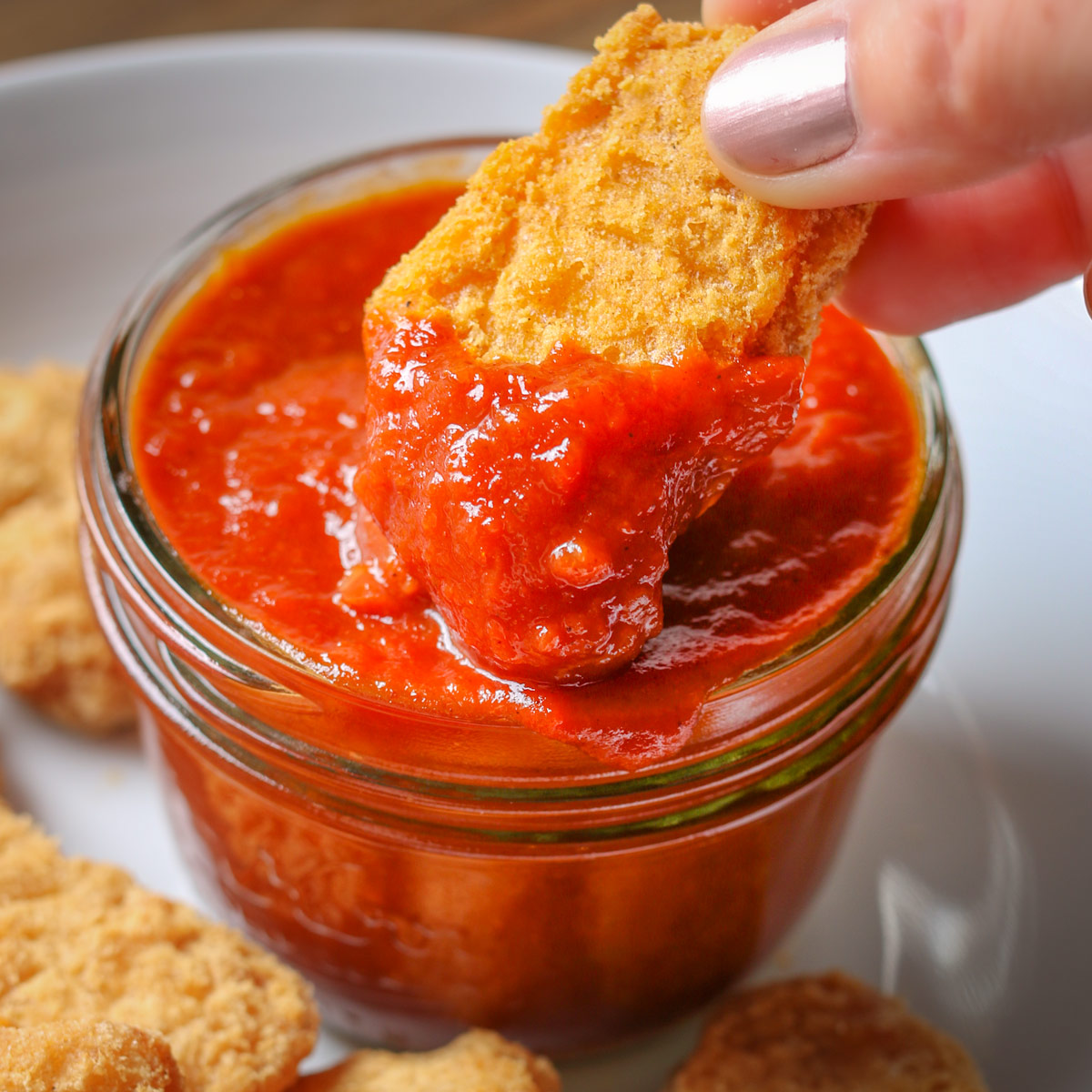 manicured hand dipping a chicken nugget into homemade apricot BBQ sauce.