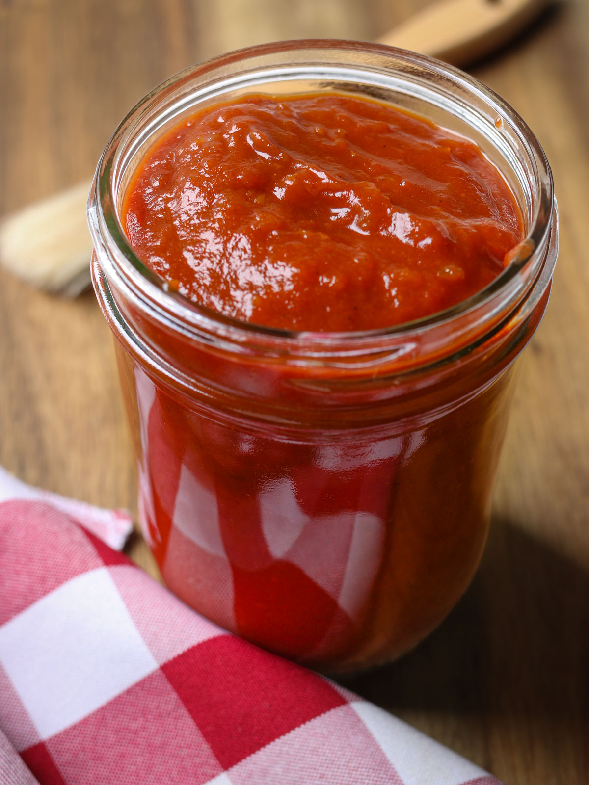 pint jar of apricot bbq sauce on board with red checked cloth and basting brush.