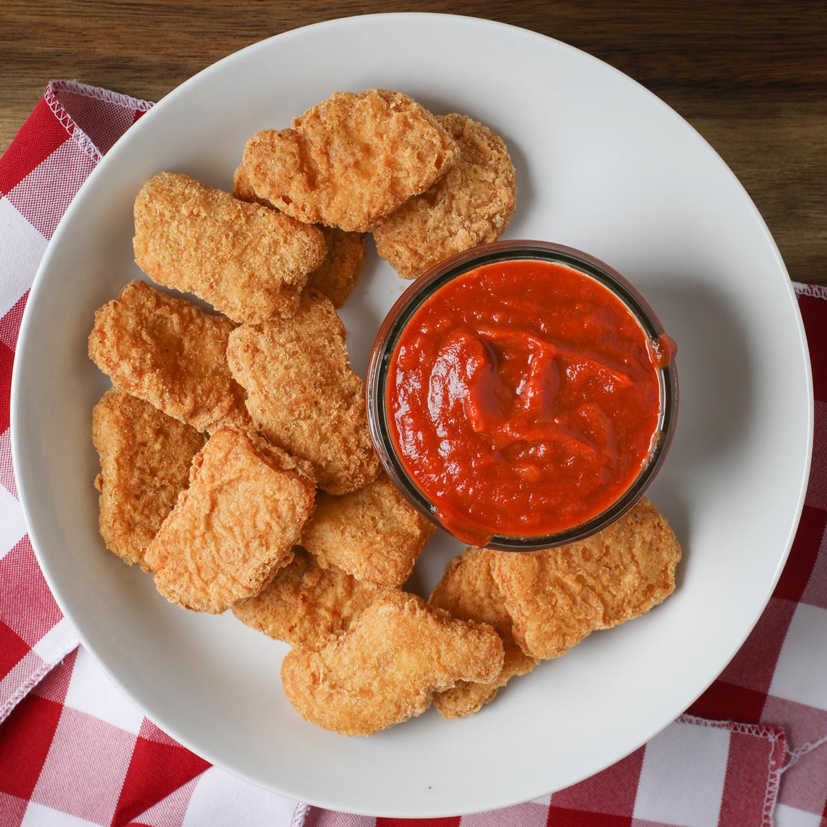 white plate of chicken nuggets on a red checked cloth with a jar of apricot bbq sauce.