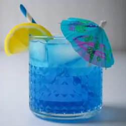 side view of blue lagoon mocktail with paper umbrella, straw, and lemon wedge.