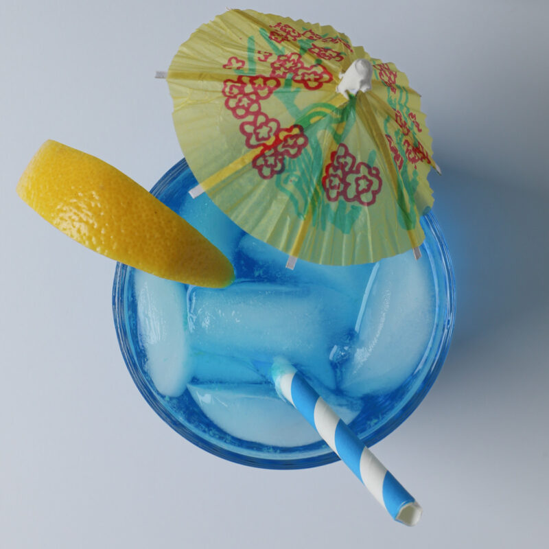 the finished blue lagoon mocktail with a lemon wedge, straw, and paper umbrella.