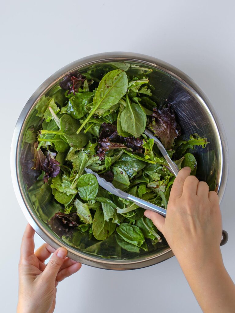 tossing the salad greens with dressing in the large steel bowl.