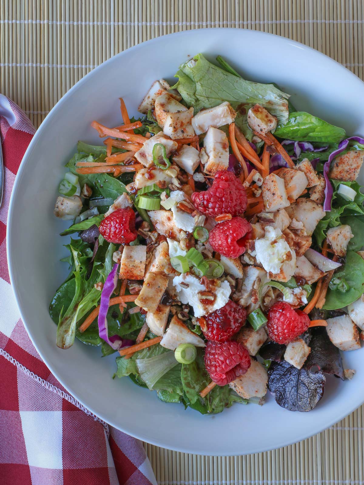 overhead shot of a salad with chicken, raspberries, and goat cheese.