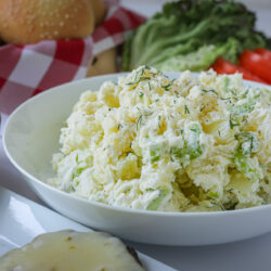 bowl of dill potato salad on a table with other picnic items.