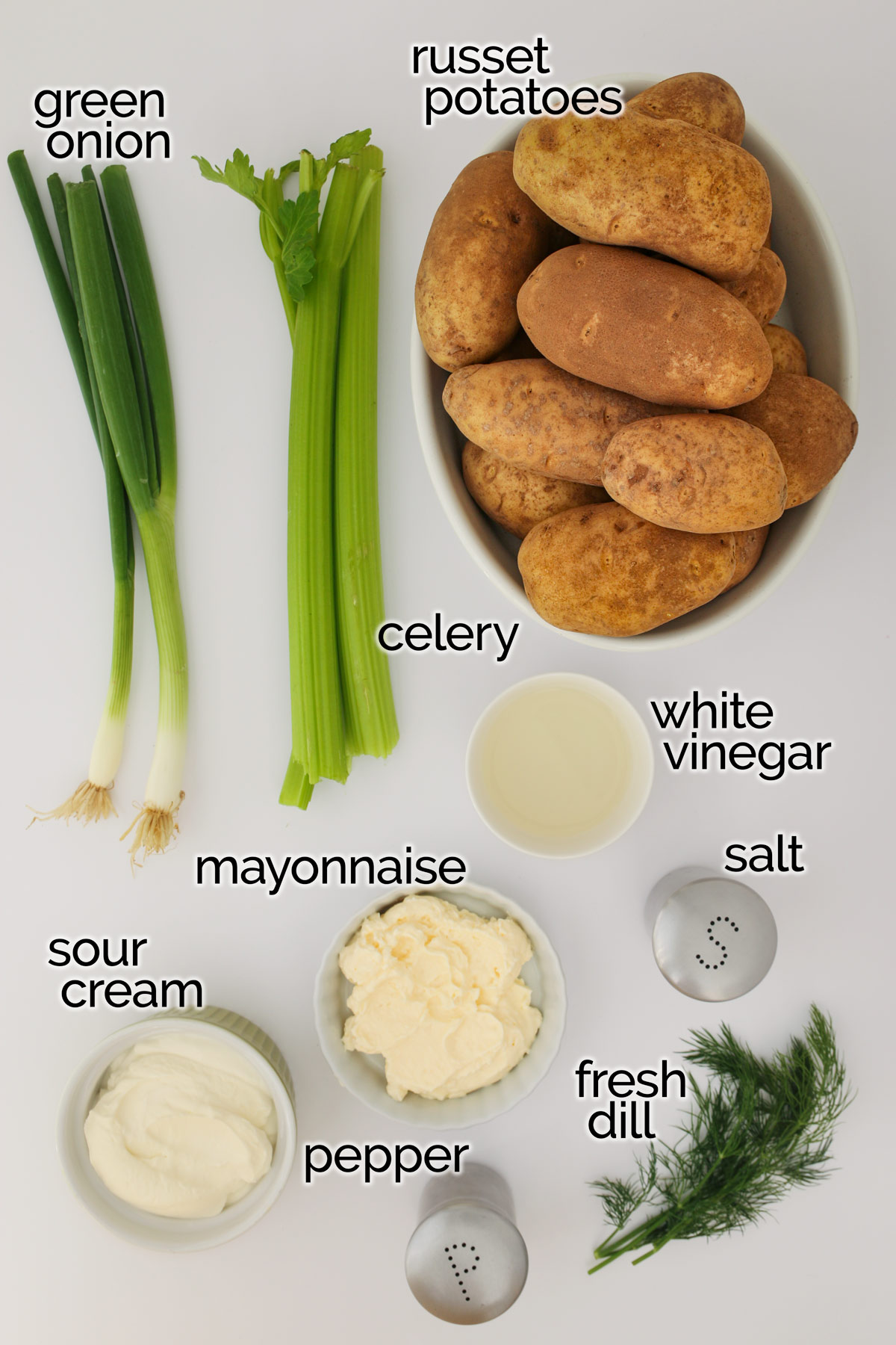 składniki sałatki ziemniaczanej z koperkiem ułożone na białym blacie.