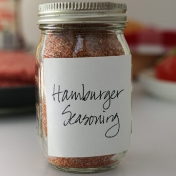 handwritten label for hamburger seasoning on a small spice jar on table with burger ingredients.