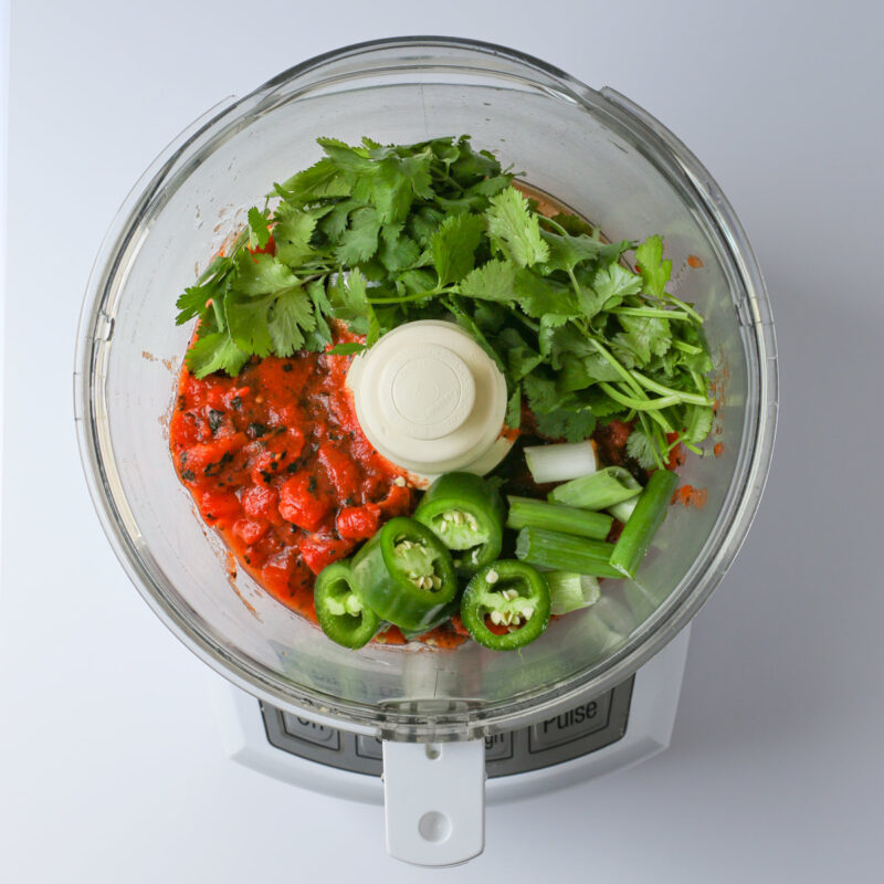 diced tomatoes, onion, jalapeno, and cilantro in the bowl of a food processor.
