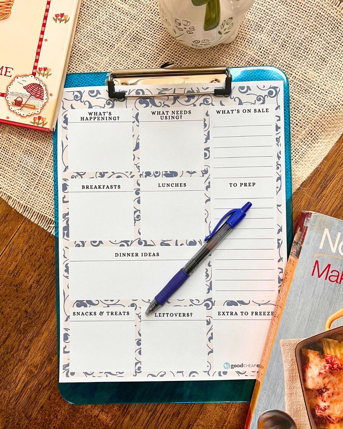 meal planner on a blue clipboard with pen on table with cookbooks