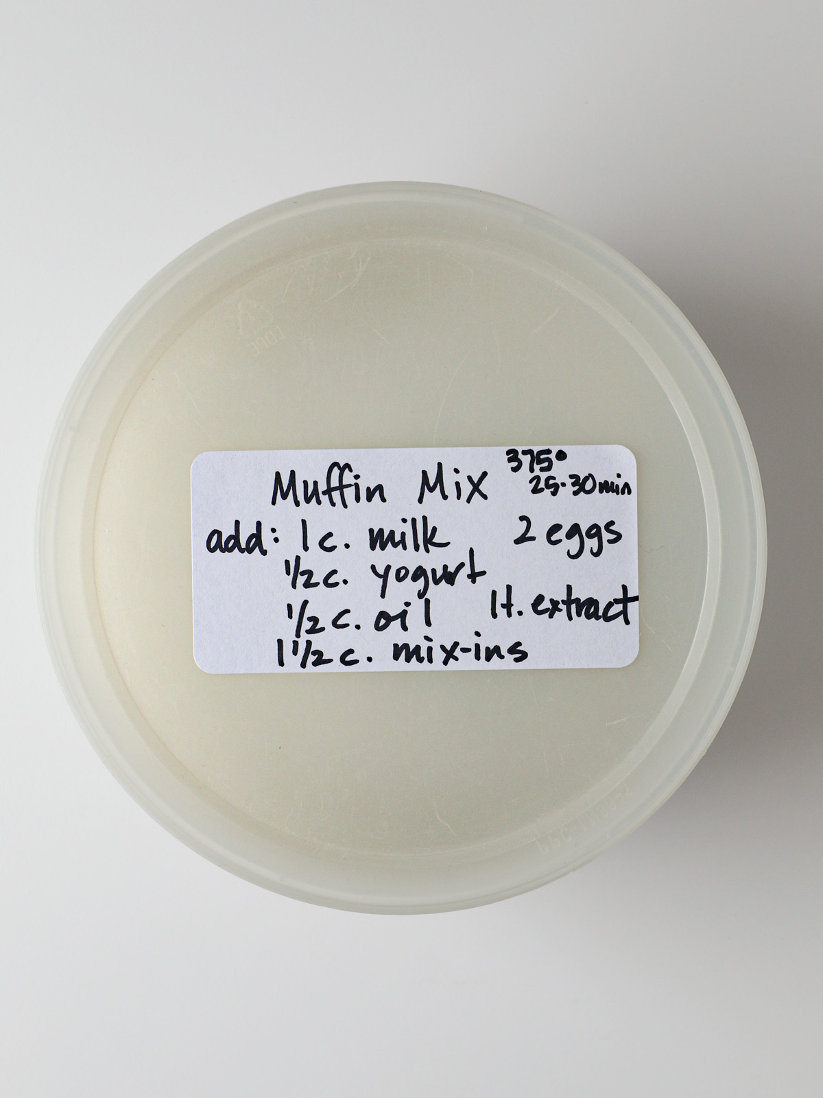 plastic tub holding homemade muffin mix with a handwritten label.