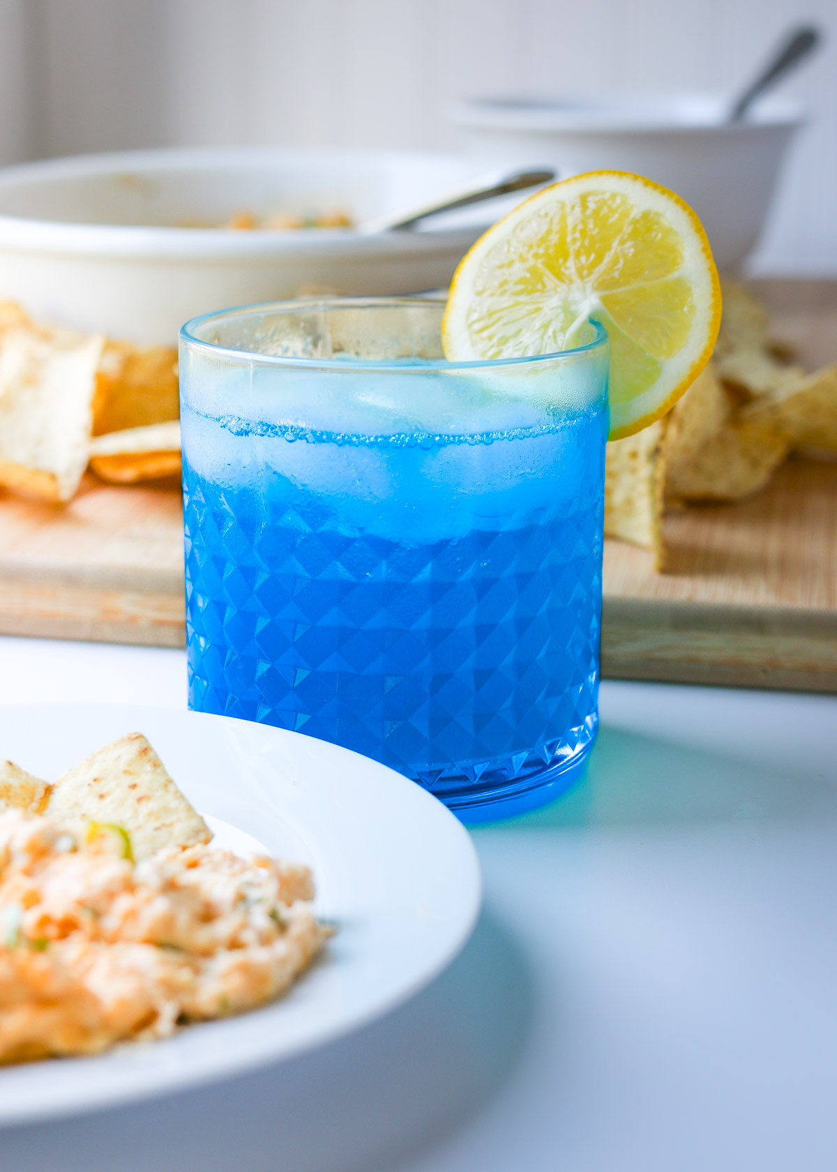 blue lagoon mocktail next to a plate of spicy chicken dip.