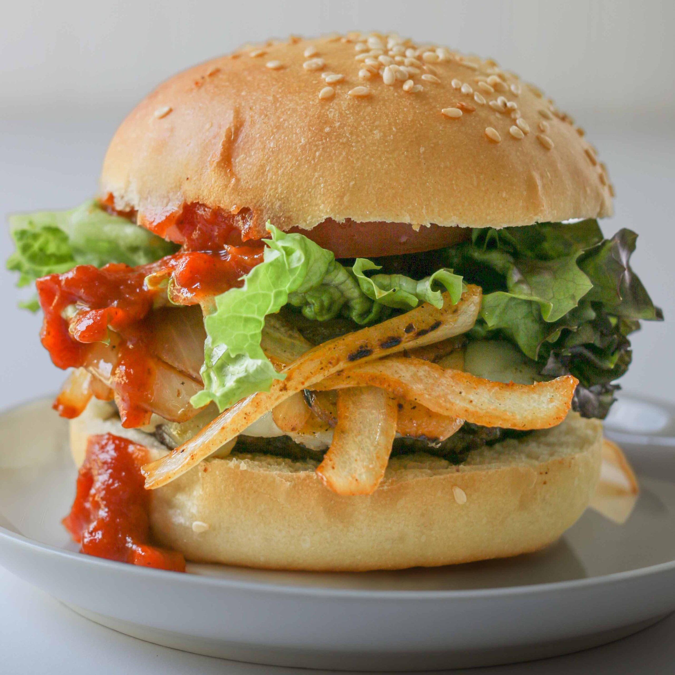 close up of BBQ bacon cheeseburger on a white plate with a white background.