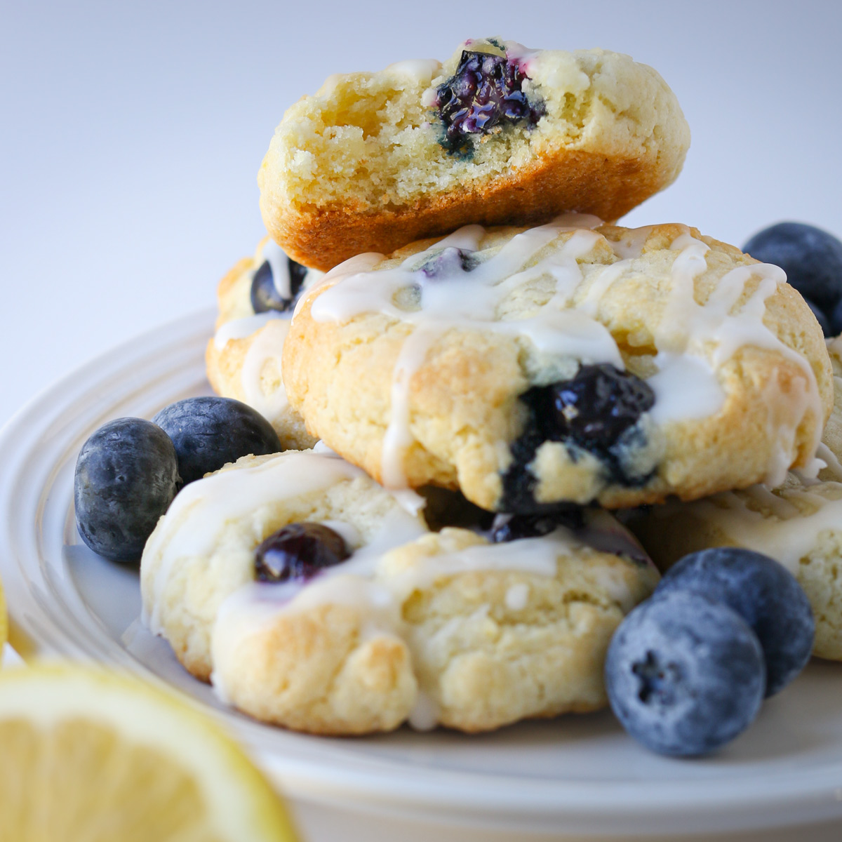 cookies stacked on white plate with fresh blueberries and a lemon round in the foreground.