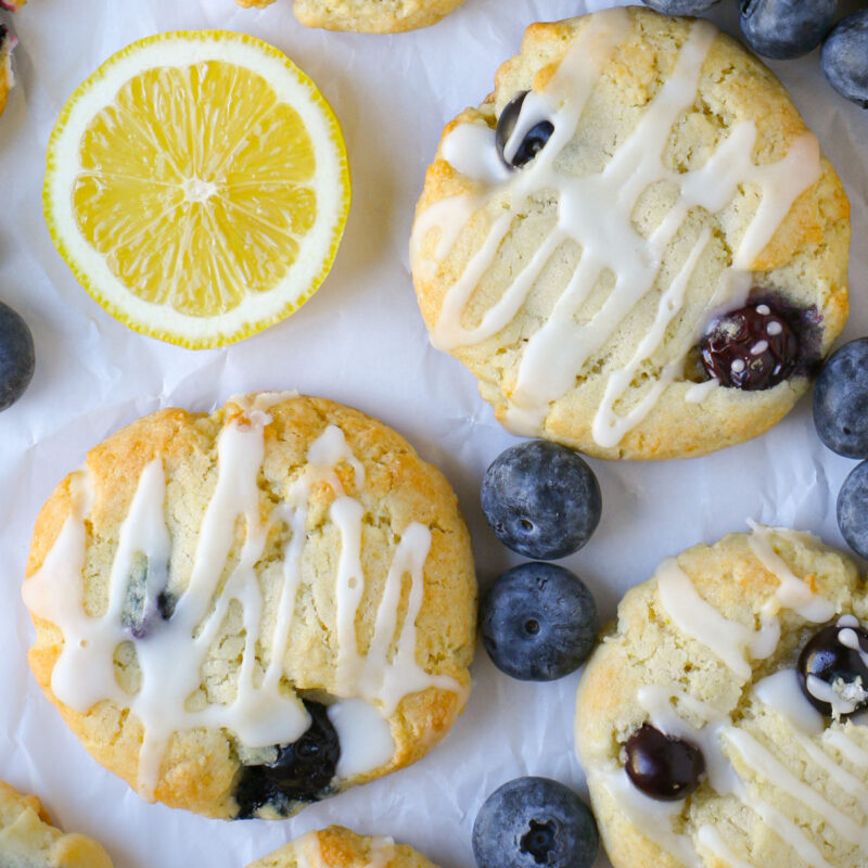 array of glazed blueberry cookies with fresh berries and lemon rounds interspersed on the parchment.